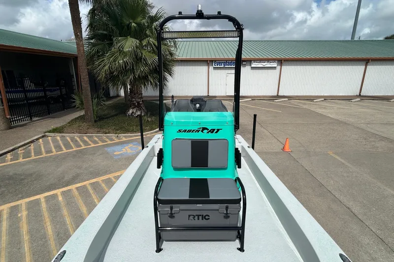 Slide: The Image of 2026 Gulf Coast Saber Cat boat with teal console and RTIC cooler, parked outdoors. - 18