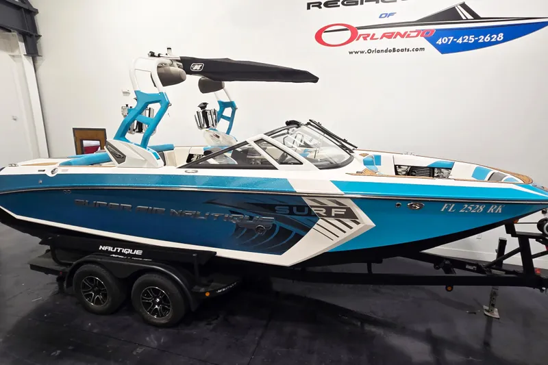 Slide: The Image of 2017 Nautique Super Air Nautique G23 boat in showroom, blue and white design, on trailer. - 2