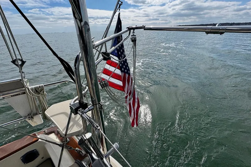 Slide: The Image of 1998 Island Packet 350 sailboat cockpit with ocean view, featuring wood trim and nautical ropes. - 57
