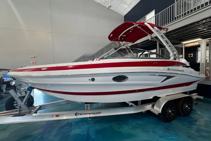 The Image of 2024 Crownline 250 XSS boat with red and white design on a trailer indoors. - 0