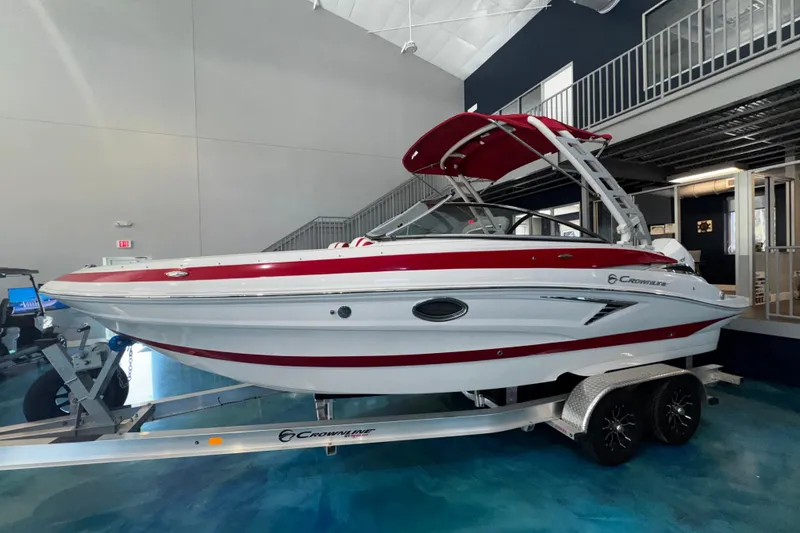 Slide: The Image of 2024 Crownline 250 XSS boat with red and white design on a trailer indoors. - 10