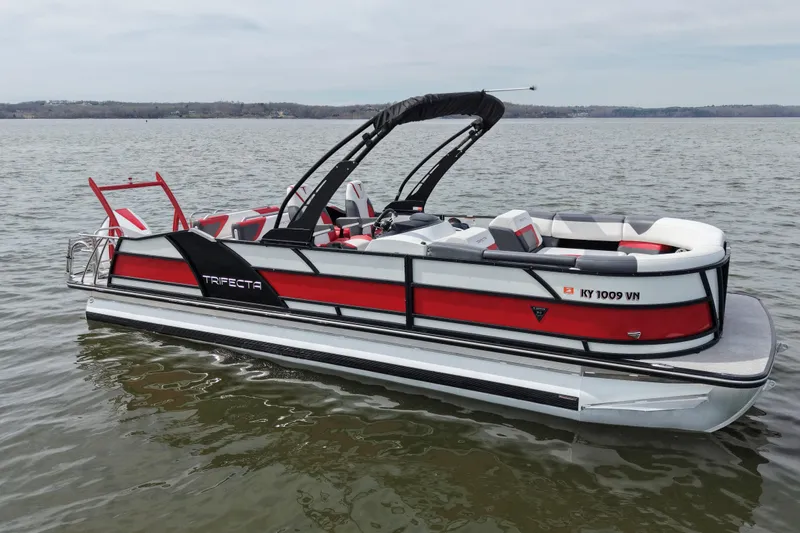 The Image of 2024 Trifecta 25ULE SS pontoon boat on calm water, featuring sleek red and white design. - 0