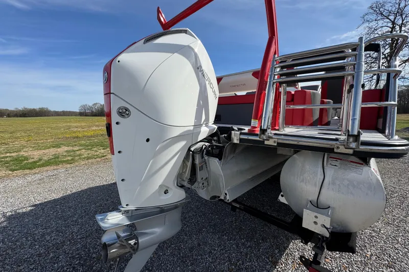 Slide: The Image of 2024 Trifecta 25ULE SS pontoon boat with Mercury outboard motor, parked on gravel. - 10