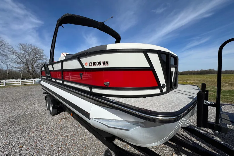 Slide: The Image of 2024 Trifecta 25ULE SS pontoon boat on trailer, red and white design, outdoor setting. - 14