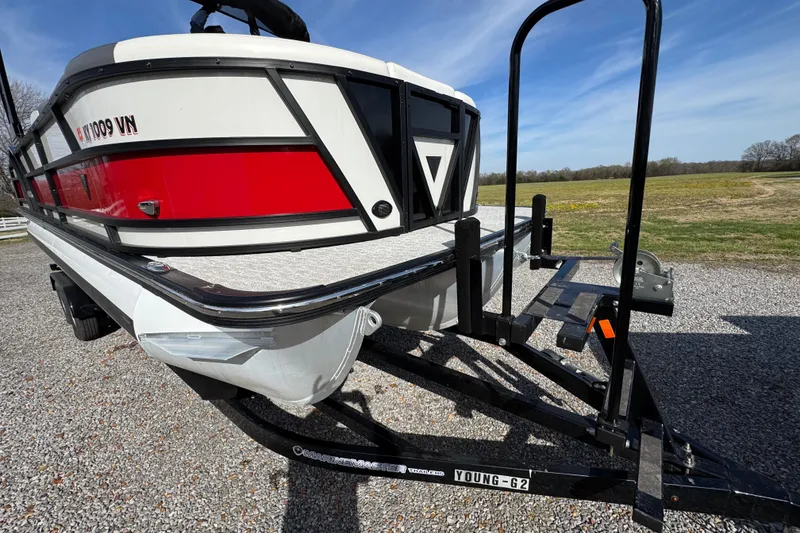 Slide: The Image of 2024 Trifecta 25ULE SS pontoon boat on trailer, parked on gravel with scenic background. - 16