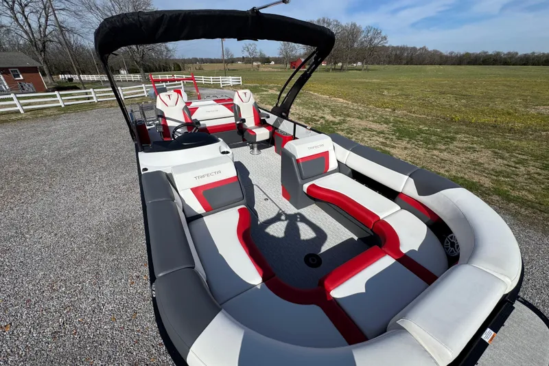 Slide: The Image of 2024 Trifecta 25ULE SS pontoon boat with red and gray seating, parked outdoors. - 44