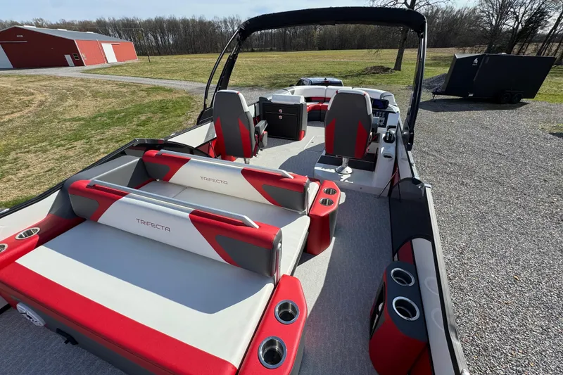 Slide: The Image of 2024 Trifecta 25ULE SS pontoon boat with red and gray seating, parked outdoors. - 56