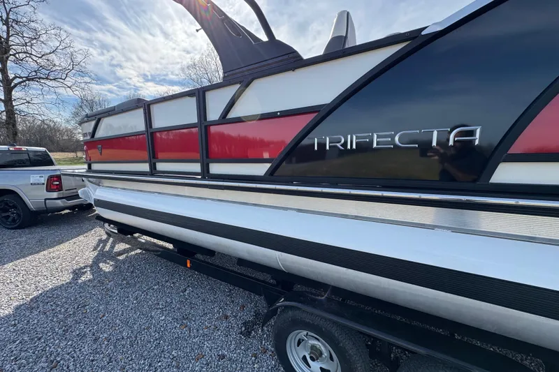 Slide: The Image of 2024 Trifecta 25ULE SS pontoon boat on trailer, parked outdoors. - 6