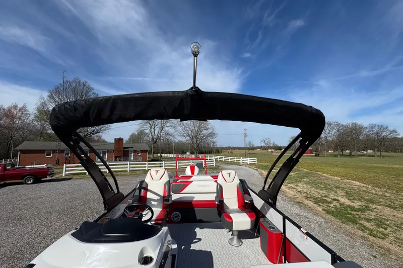 Slide: The Image of 2024 Trifecta 25ULE SS pontoon boat with red and white seating, parked outdoors. - 62