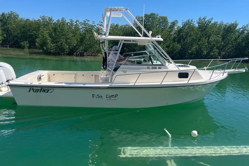 The Image of 2005 Parker 2510 Modified Vee Walkaround boat on calm water, surrounded by greenery. - 1
