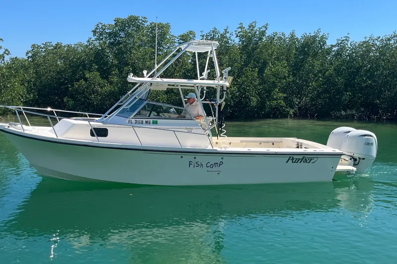 Slide: The Image of 2005 Parker 2510 Modified Vee Walkaround boat on calm water, surrounded by lush greenery. - 8