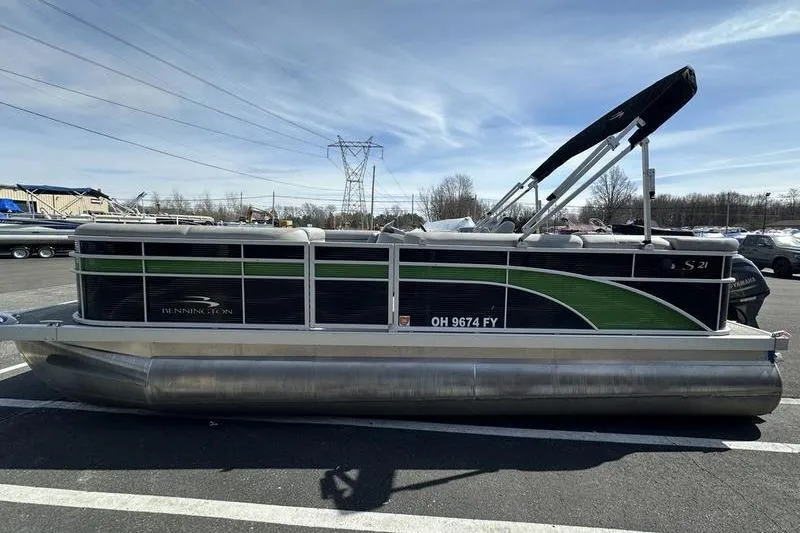 Slide: The Image of 2020 Bennington 21 SL pontoon boat with green and black design, parked outdoors. - 8