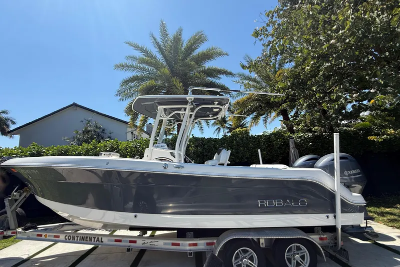 The Image of 2017 Robalo R242 Center Console boat on trailer, surrounded by palm trees. - 1
