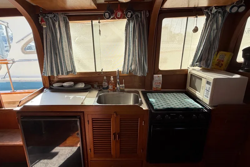 Slide: The Image of 1985 Albin 36 Trawler kitchen with sink, stove, microwave, and window curtains. - 21