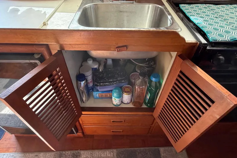 Slide: The Image of Open cabinet under sink in 1985 Albin 36 Trawler, containing cleaning supplies and bottles. - 26