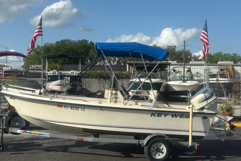 The Image of 2000 Key West 1720 Center Console boat with blue canopy on trailer, American flags in background. - 0