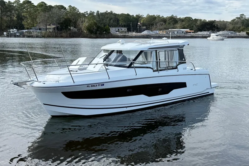 The Image of 2025 Jeanneau NC 1095 Coupe boat cruising on a calm lake with wooded shoreline. - 1