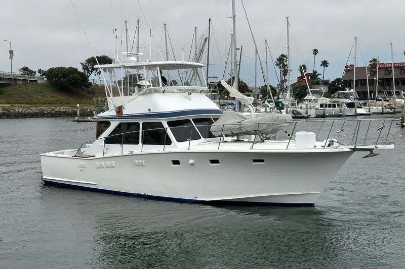 The Image of 1976 Pacifica Flybridge yacht docked in a marina, surrounded by sailboats and palm trees. - 0