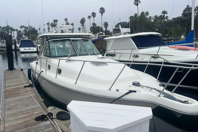 Slide: The Image of 2005 Pursuit 3100 Offshore boat docked at a marina with palm trees in the background. - 3
