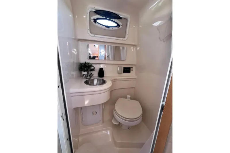 Slide: The Image of 2008 Larson Cabrio 260 boat bathroom with sink, toilet, mirror, and porthole window. - 12