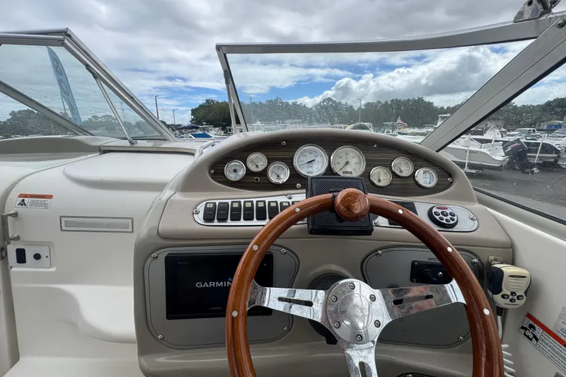 Slide: The Image of 2008 Larson Cabrio 260 boat dashboard with steering wheel and gauges, under a cloudy sky. - 21