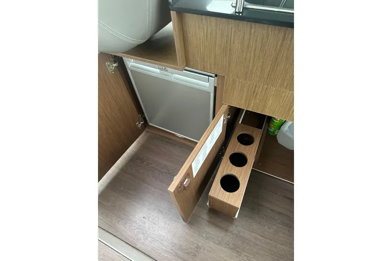 Slide: The Image of Interior of 2023 Beneteau Antares 9 showing wooden cabinetry and compact refrigerator. - 15