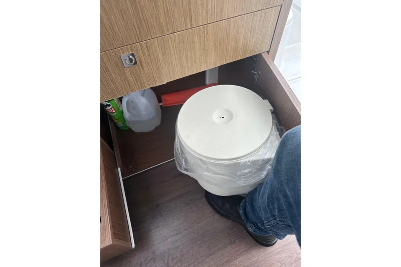 Slide: The Image of Storage compartment in 2023 Beneteau Antares 9 with cleaning supplies and trash bin. - 28