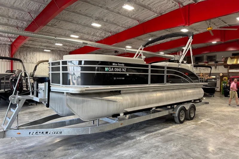 The Image of 2024 Harris Cruiser 230 pontoon boat on trailer in spacious indoor facility. - 1