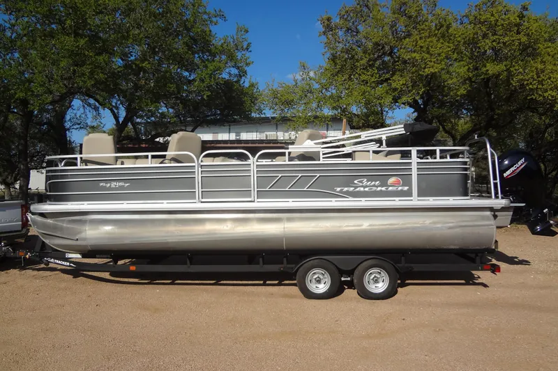 Slide: The Image of 2022 TRACKER MARINE Party Barge 24 DLX pontoon boat on trailer, surrounded by trees. - 16