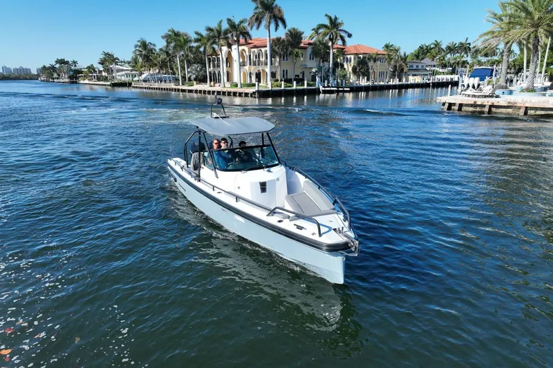 Slide: The Image of 2021 Axopar 28 T-Top boat cruising on a sunny waterfront with palm trees. - 12