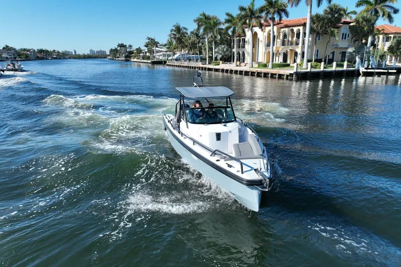 Slide: The Image of 2021 Axopar 28 T-Top cruising on a scenic waterway with palm trees and luxury homes. - 13