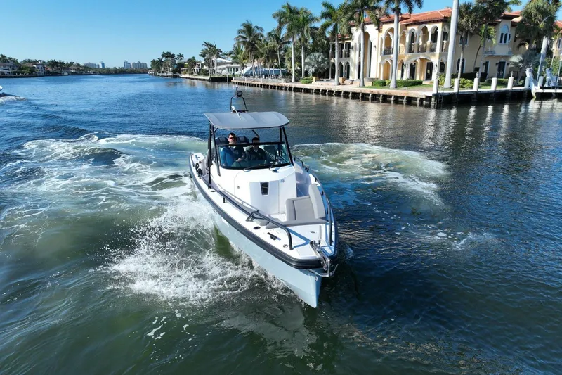 Slide: The Image of 2021 Axopar 28 T-Top cruising on a scenic waterway near luxury homes. - 14