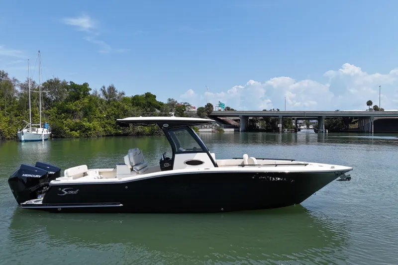 Slide: The Image of 2025 Scout 277 LXF boat on calm water near a bridge and trees. - 2