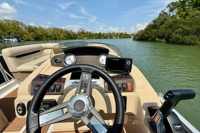 Slide: The Image of 2022 Hurricane FunDeck 2260 REF boat dashboard with steering wheel and controls on a scenic waterway. - 15