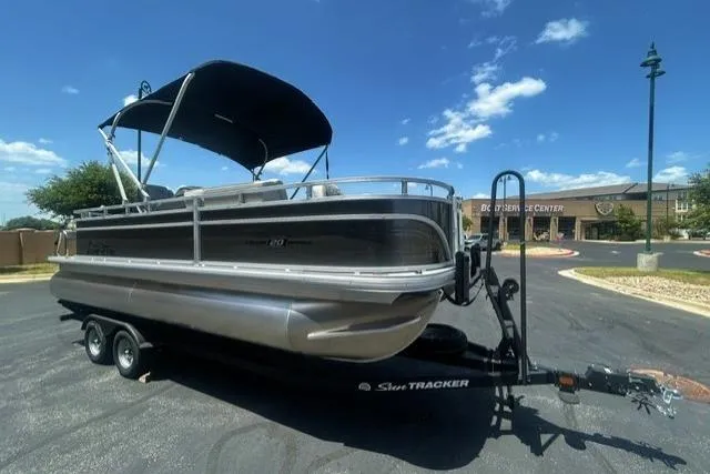 Slide: The Image of 2026 Sun Tracker Fishin' Barge 20 DLX pontoon boat on trailer under clear blue sky. - 2
