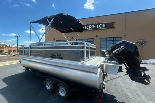 Slide: The Image of 2026 Sun Tracker Fishin' Barge 20 DLX pontoon boat with Mercury engine, parked outside service center. - 1