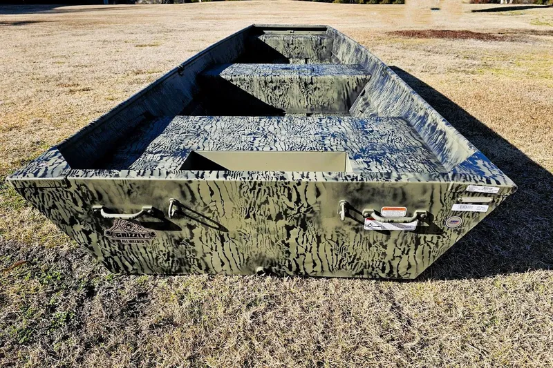 Slide: The Image of 2026 Tracker Grizzly 15 Jon boat with camouflage pattern on grassy field. - 2