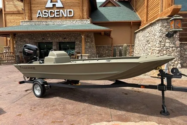 The Image of 2026 Tracker Grizzly 1648 SC boat on trailer outside rustic building. - 0