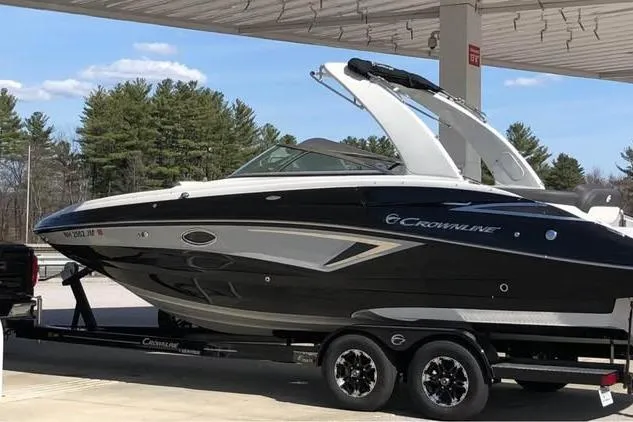 Slide: The Image of 2020 Crownline Eclipse E255 boat on trailer at a gas station, surrounded by trees. - 2