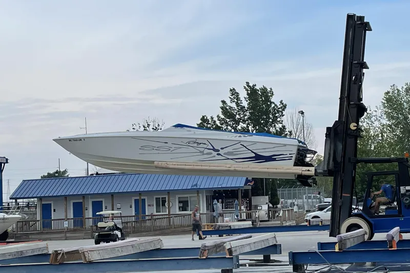 The Image of 2000 Baja 33 Outlaw boat lifted by forklift at marina. - 0