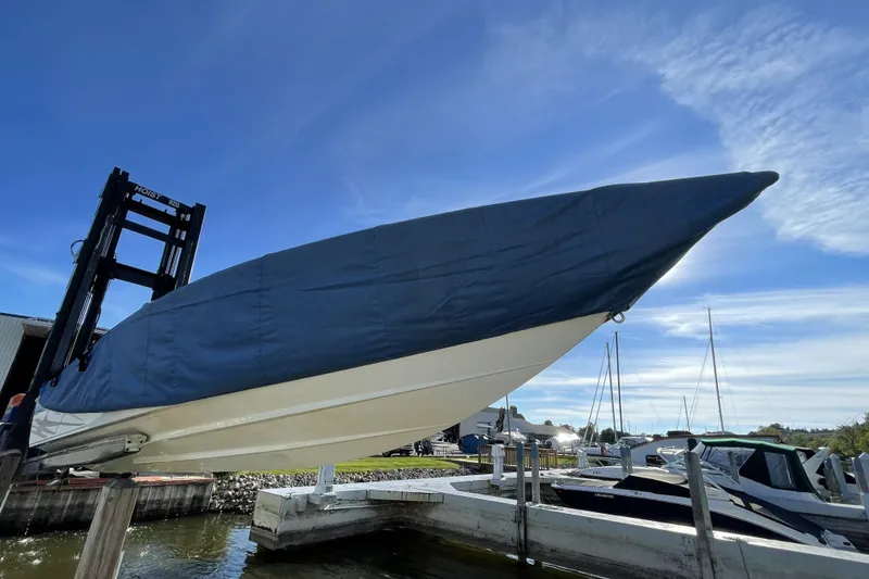 Slide: The Image of Covered 2000 Baja 33 Outlaw boat lifted by hoist at marina under blue sky. - 10