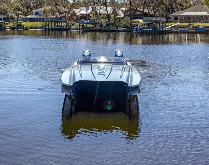 Slide: The Image of 2024 MTI 390X boat on a calm lake, surrounded by trees and houses. - 2