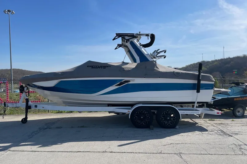 The Image of 2022 Centurion Ri230 boat on trailer, covered, with blue and white design, parked outdoors. - 1