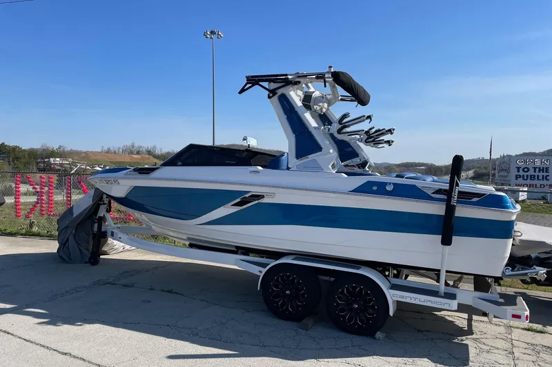 Slide: The Image of 2022 Centurion Ri230 boat on trailer, blue and white design, parked outdoors. - 13
