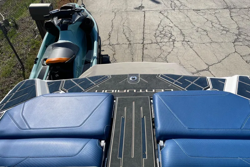 Slide: The Image of 2022 Centurion Ri230 boat with blue seating, parked beside a jet ski on cracked pavement. - 9