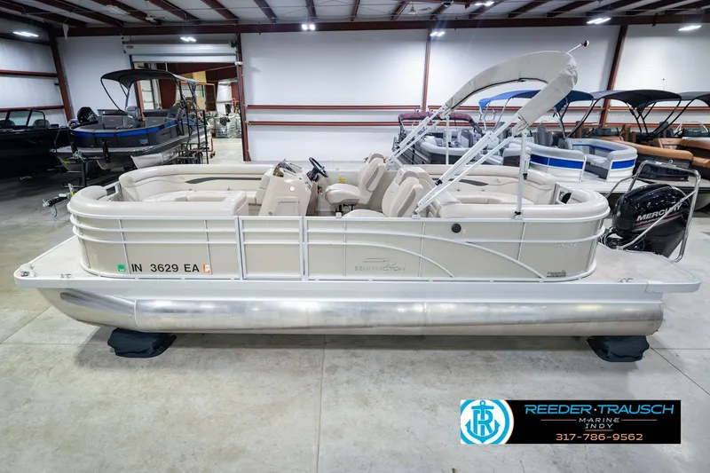 The Image of 2018 Bennington 23 SSRX pontoon boat in showroom, featuring beige seating and Mercury outboard motor. - 2