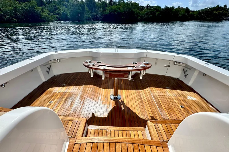 Slide: The Image of 2017 Viking 52 Sport Tower boat deck with wooden flooring, overlooking serene water and lush greenery. - 24