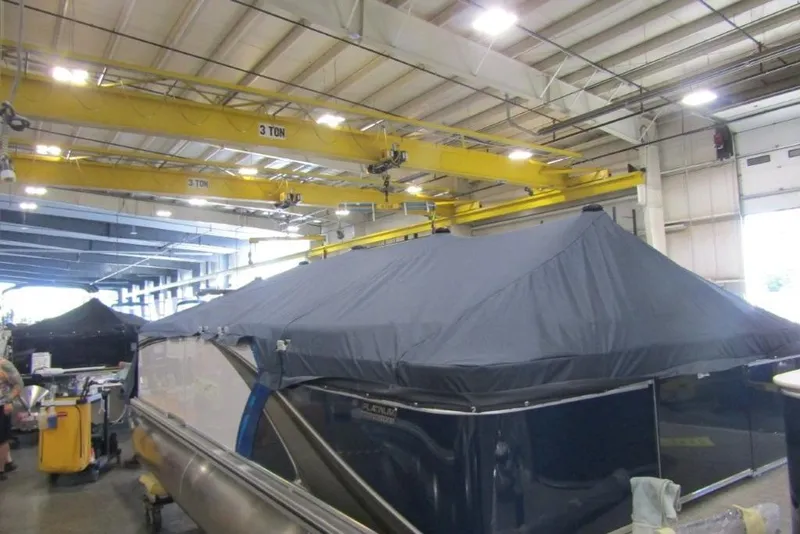 Slide: The Image of 2026 Tahoe Pontoon LTZ Quad Lounger 23 covered in a warehouse with overhead cranes. - 14