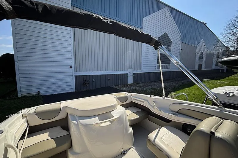 Slide: The Image of 2004 Sea Ray 185 Sport boat interior with beige seating, near a large metal building. - 8