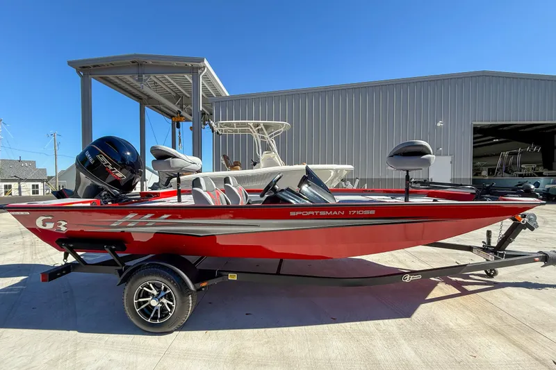 The Image of 2026 G3 Sportsman 1710 SE boat in red, parked outdoors near a warehouse. - 1